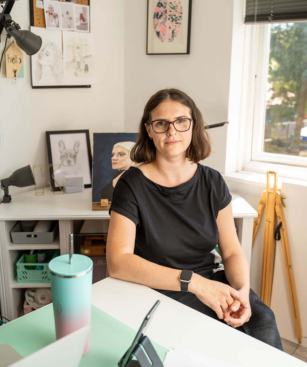Kirsty sitting at a desk in a home office with artwork on the wall.